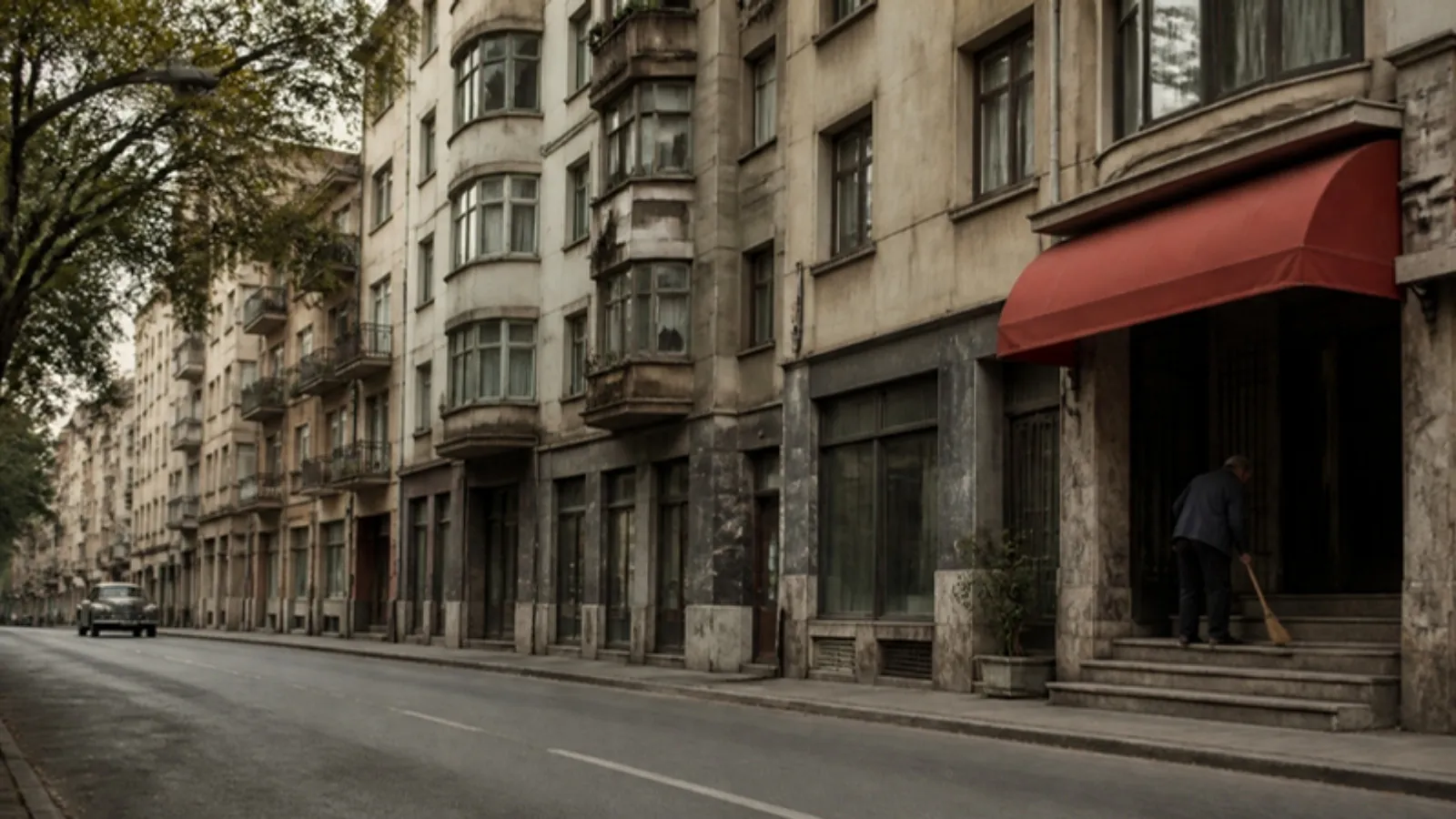 Zemin katında dükkânlar bulunan eski apartmanlar ve girişi süpüren kapıcı