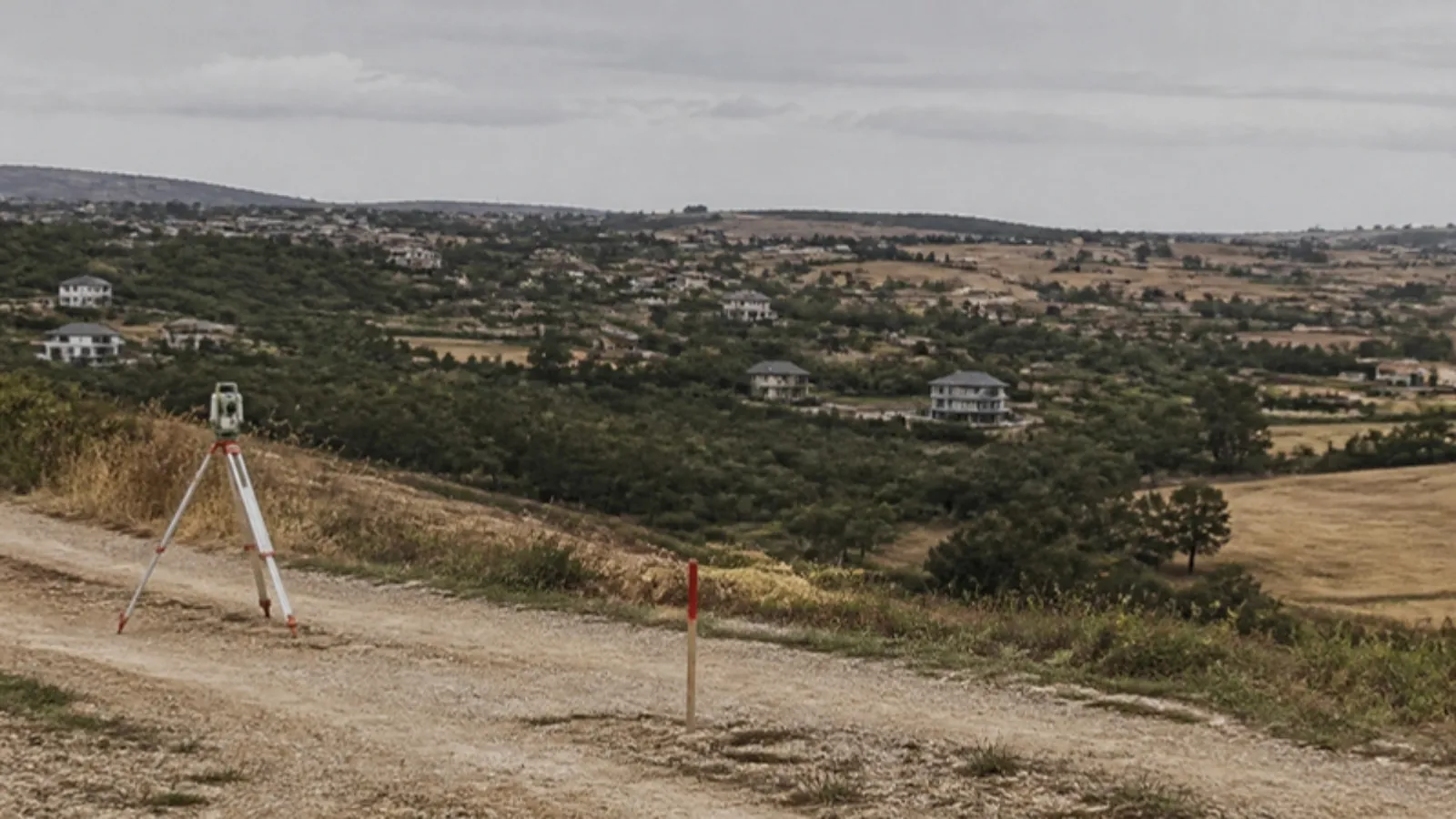 Tarım alanları arasında dağınık evler ve toprak yolda ölçüm sehpası