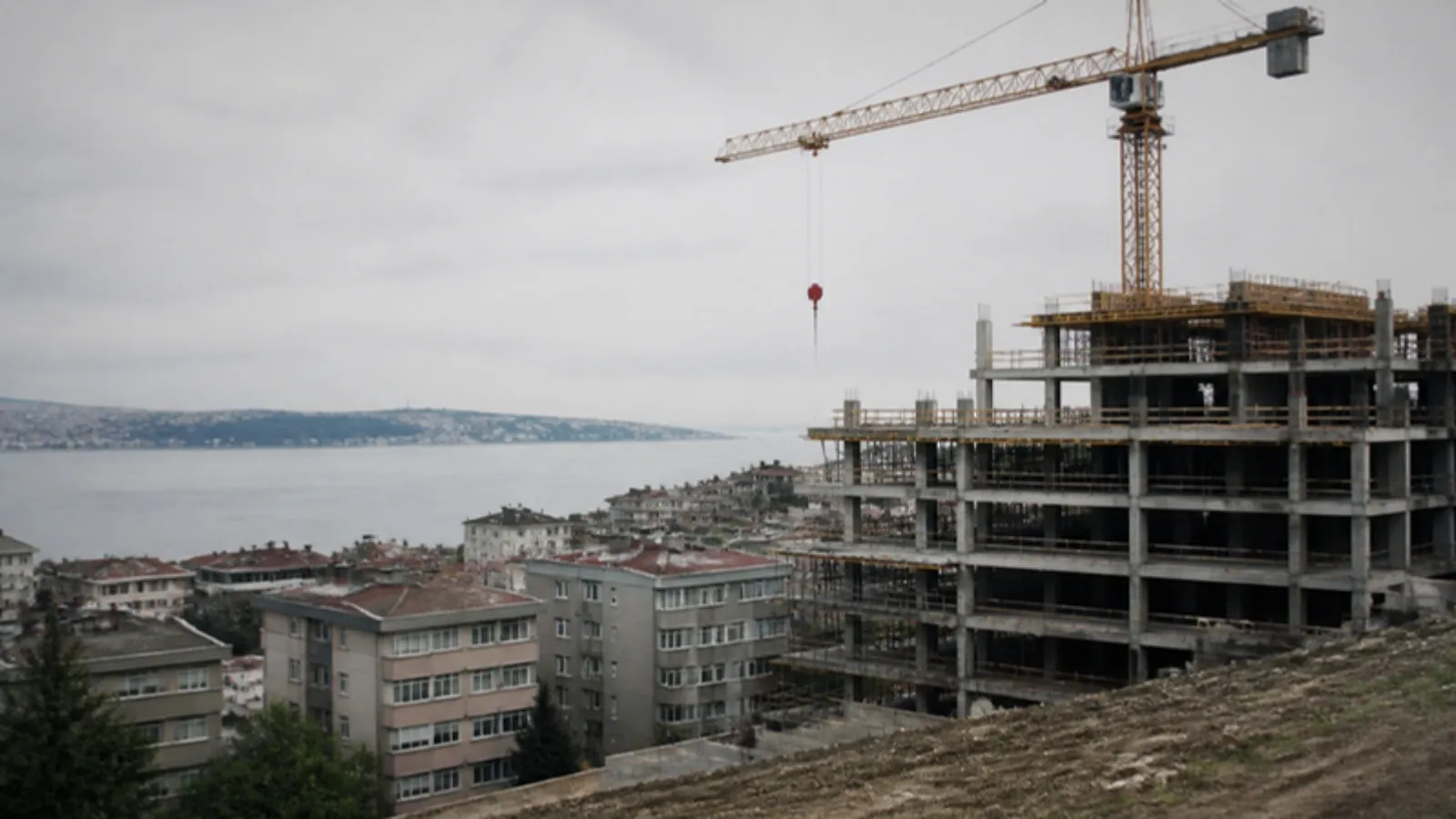 Göl kıyısına yakın yamaçta eski apartmanlar ve yanında yükselen yeni bina