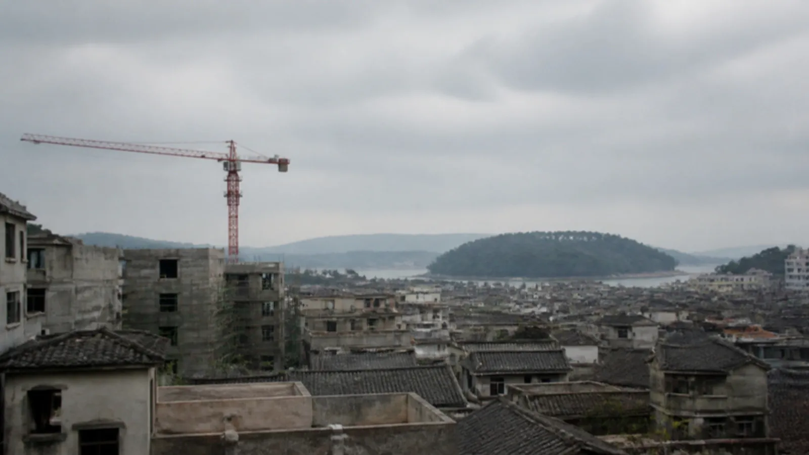 Yamaçta eski yapılar, yeni inşaatlar ve uzakta ormanlık havza